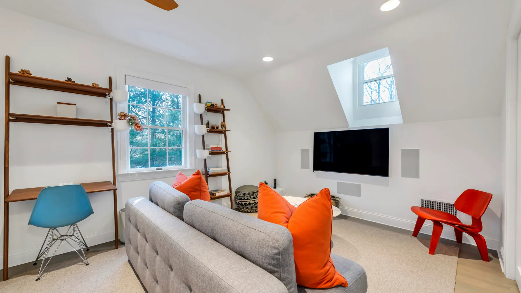 A bright living room with a television, gray seating, and orange cushions.