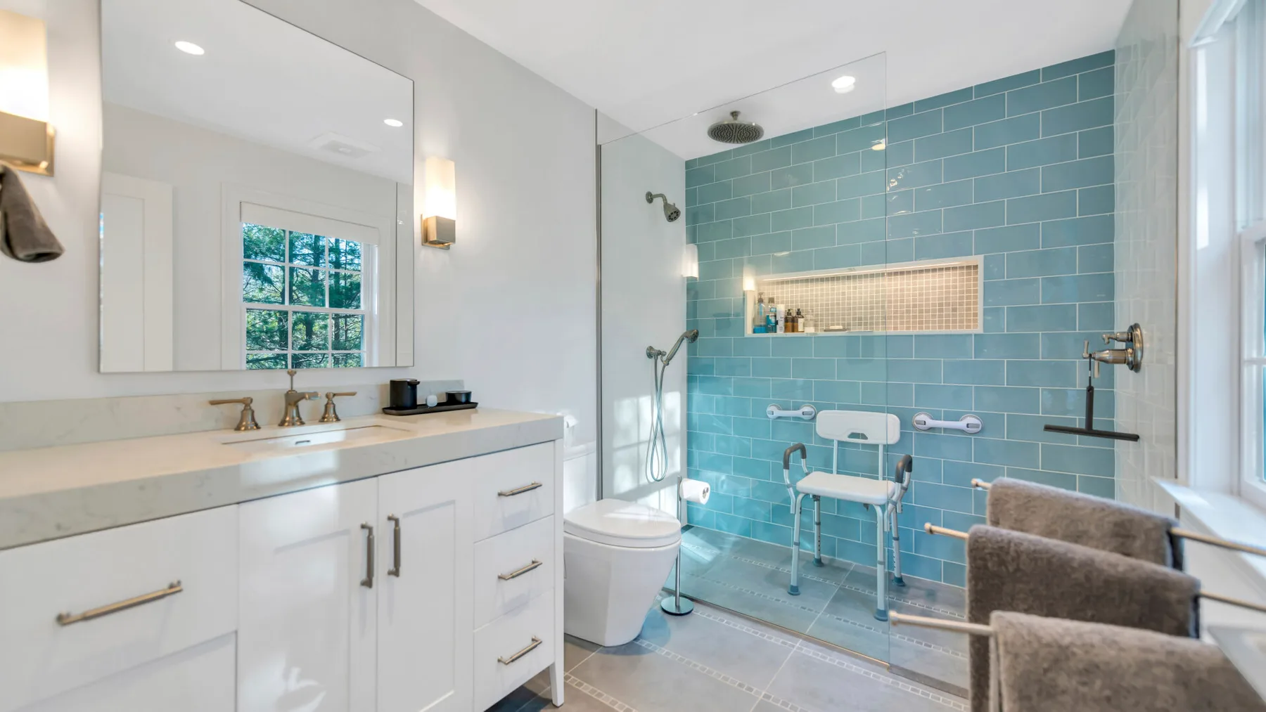 A bright bathroom with a vanity, toilet, and blue-tiled shower area.