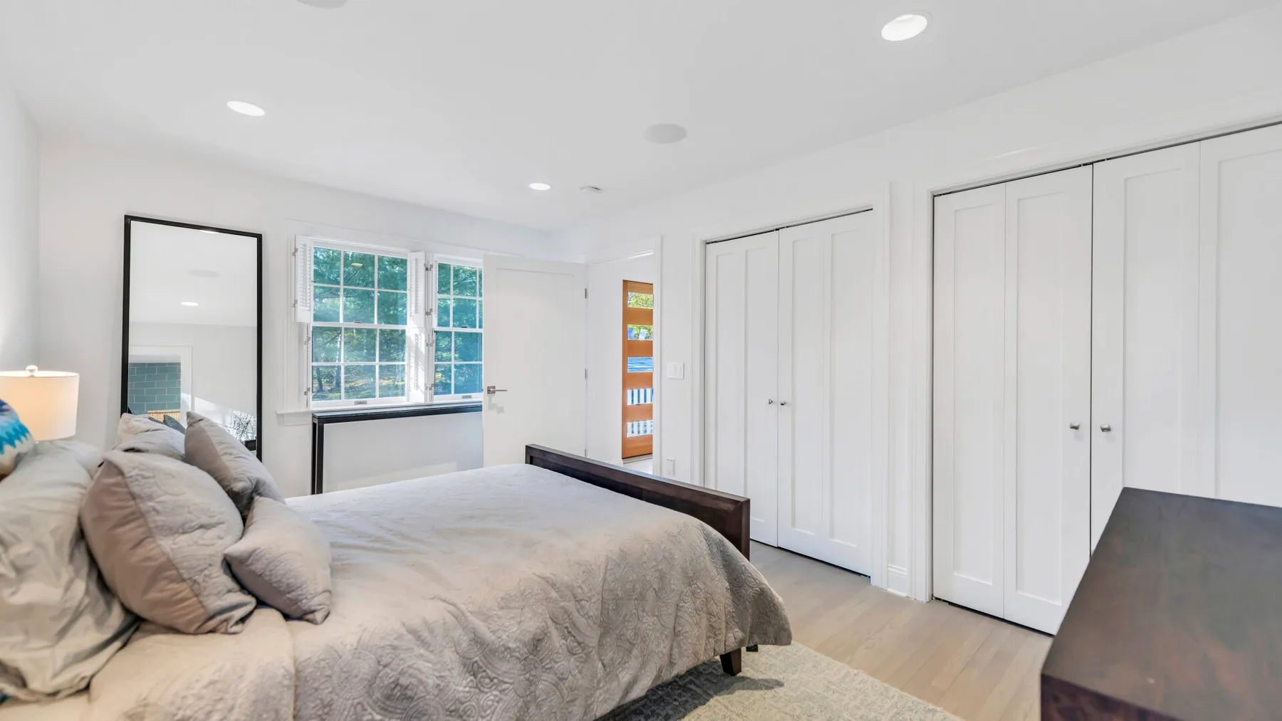 A bright bedroom with a bed beside a large window and white closets.