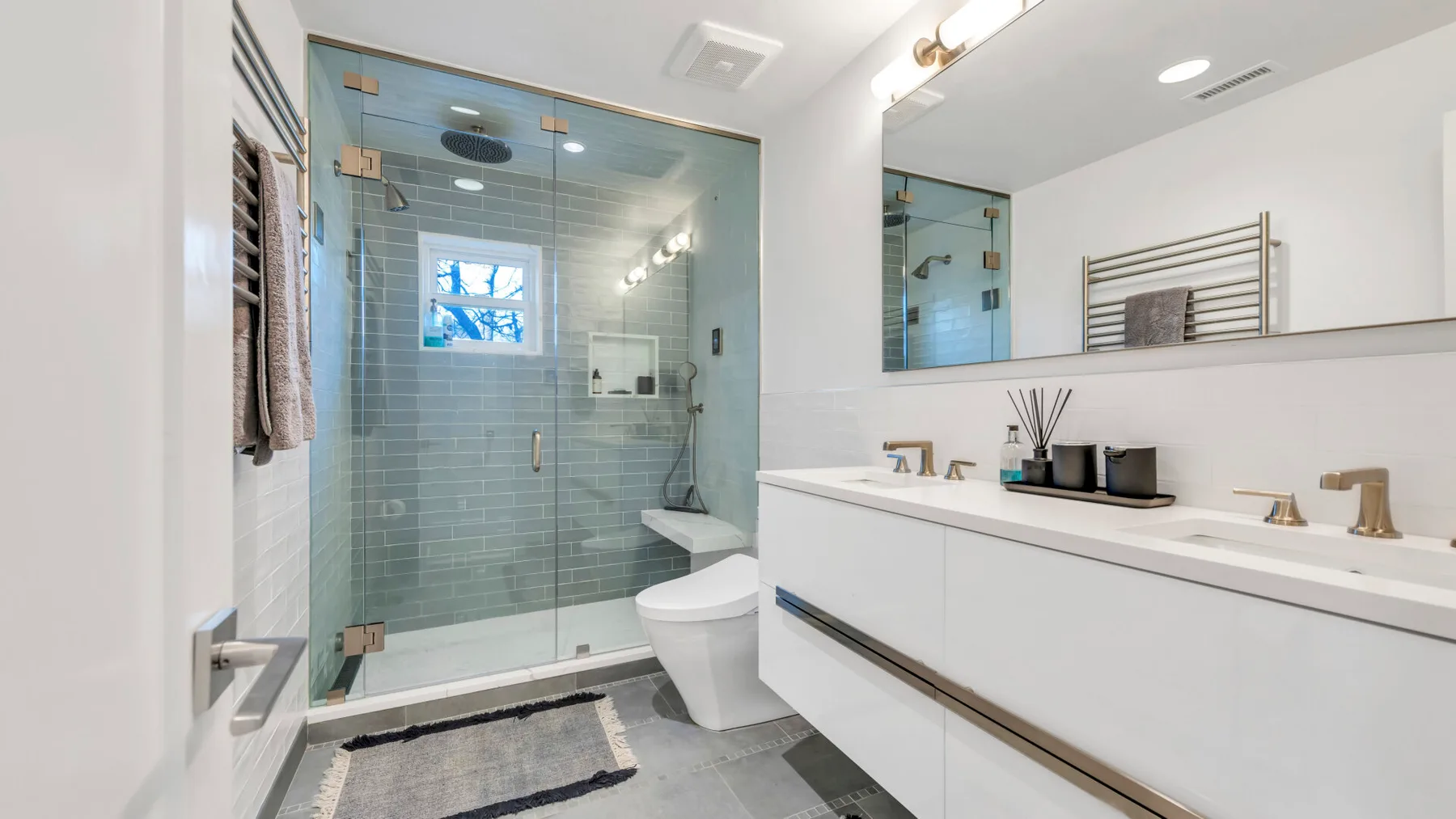 A bright bathroom with a glass shower, bathtub, and long vanity.