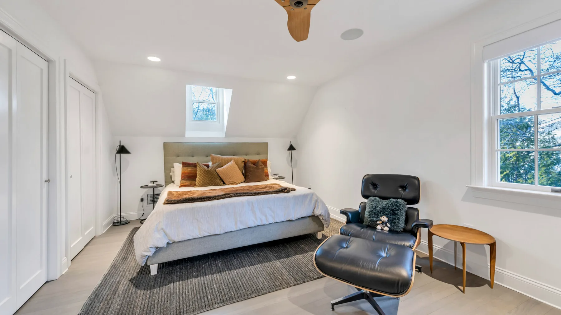 A bright bedroom with a bed and a dark lounge chair beside the window.