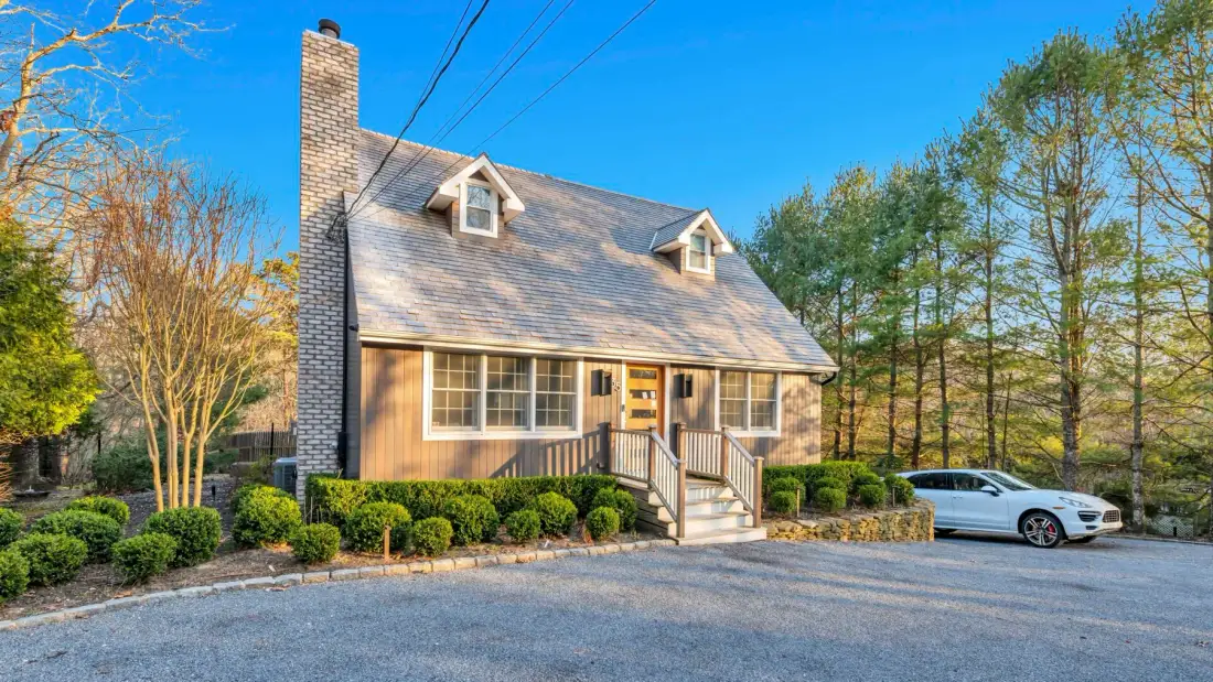 A house with a sloped roof, shrubs, and a car parked nearby.