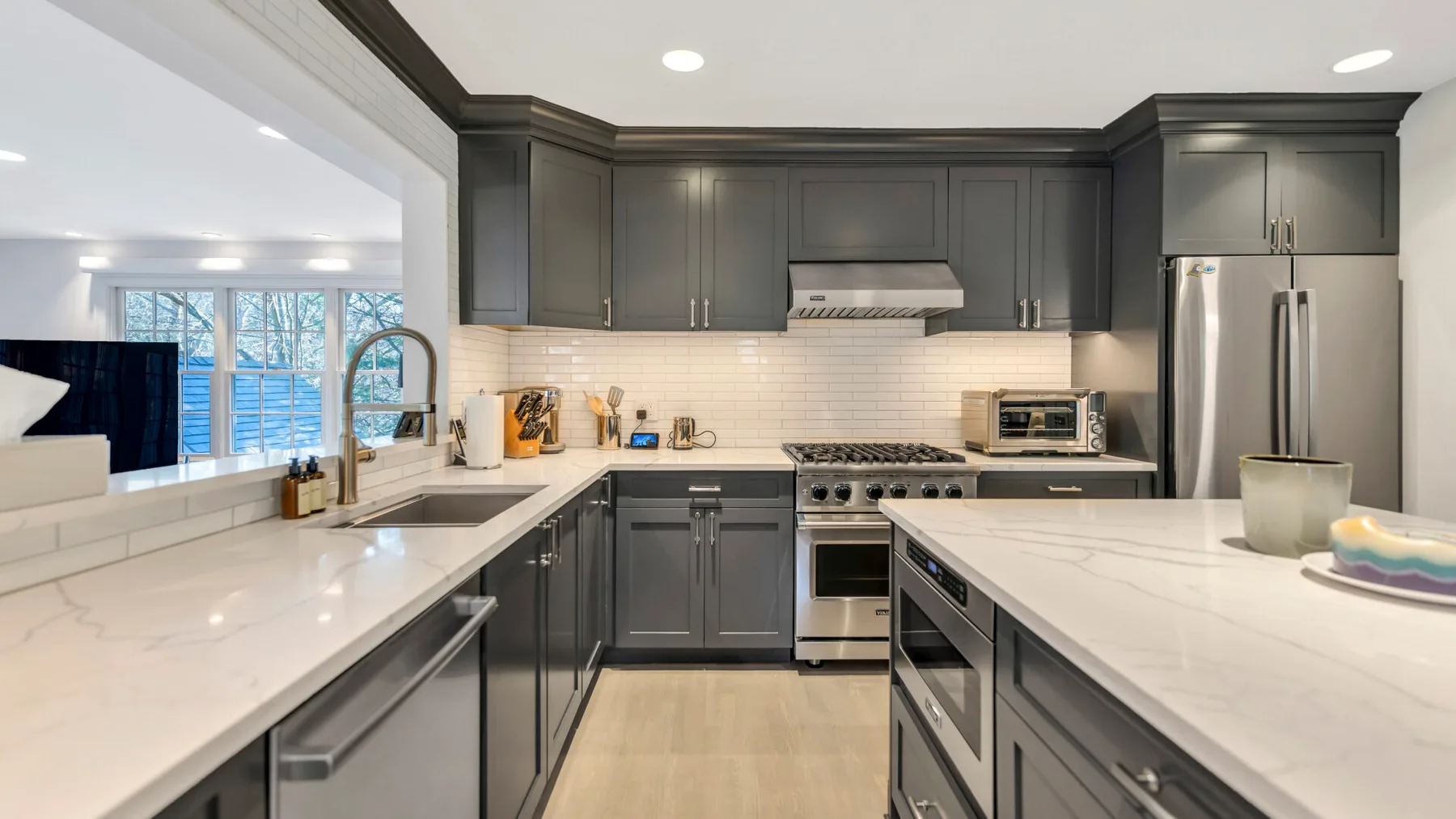 A modern kitchen with dark cabinets, light countertops, and stainless steel appliances.