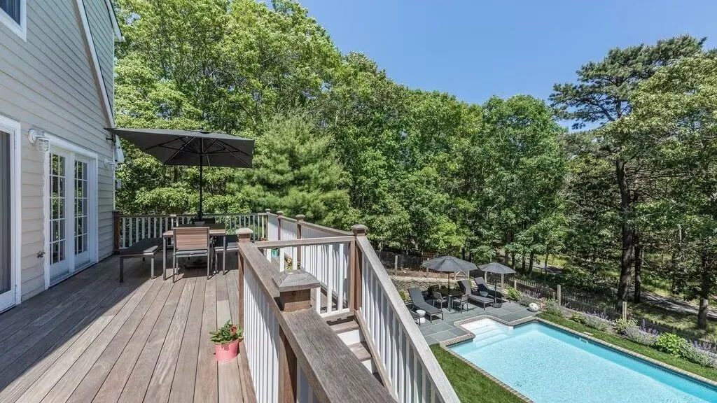 A wooden deck overlooks an outdoor swimming pool surrounded by trees.