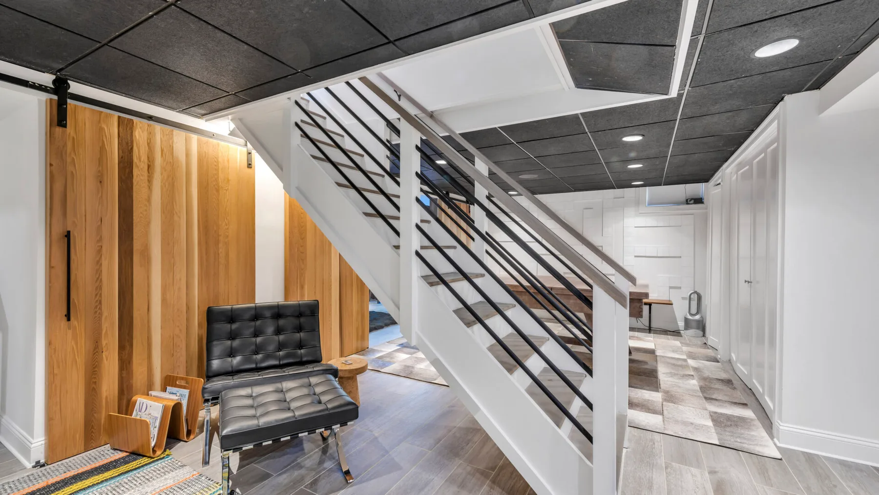 A modern interior hallway with a staircase and a black bench beside wood-paneled walls.