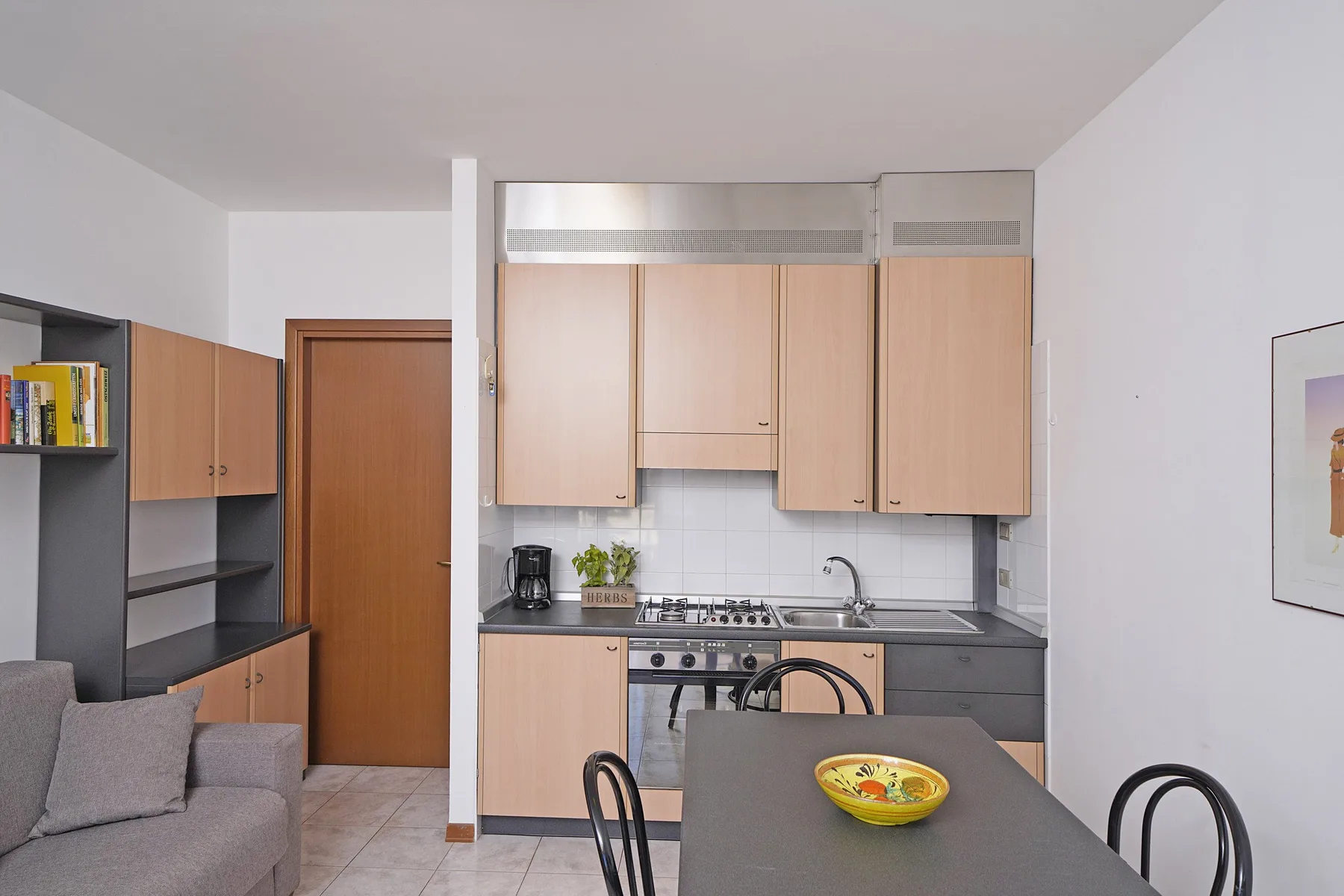 A compact kitchen with light wood cabinets opens onto a dining table and seating area.