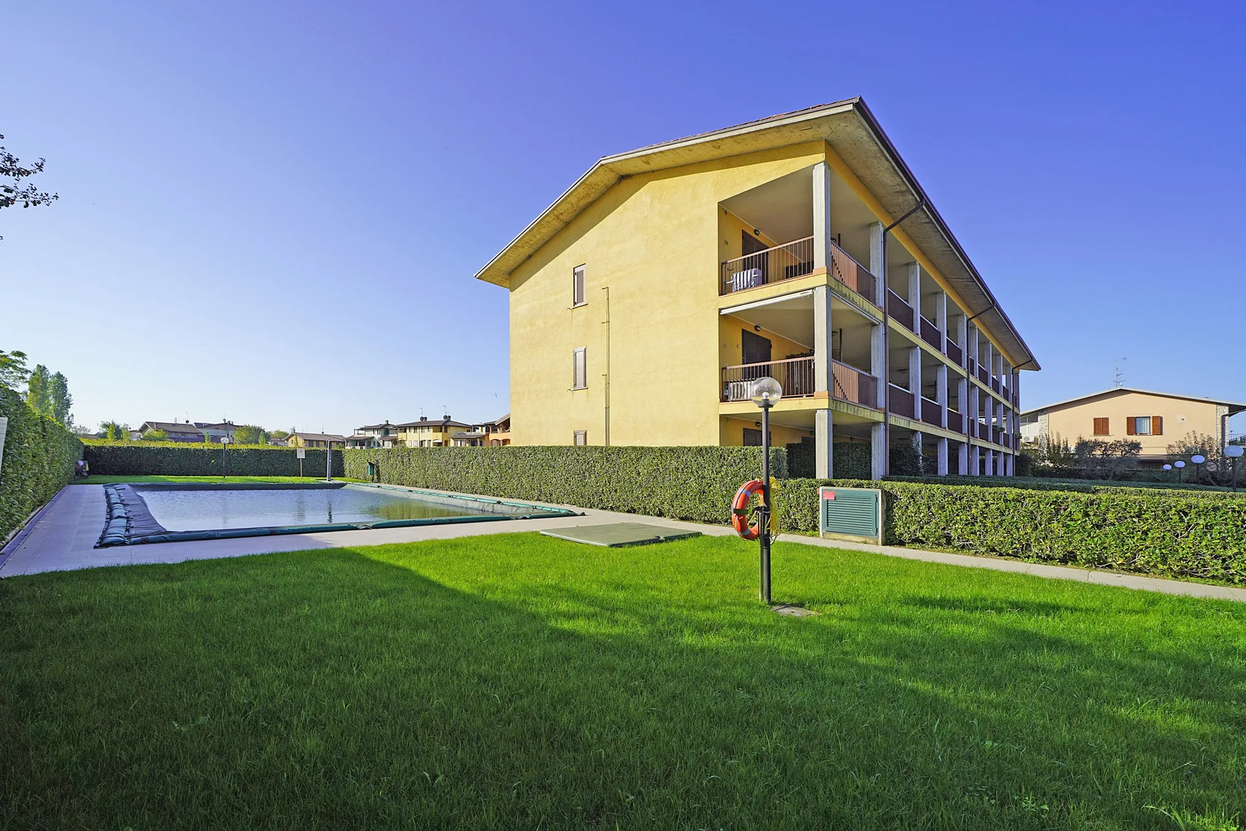 A yellow apartment building stands beside a swimming pool and green lawn.