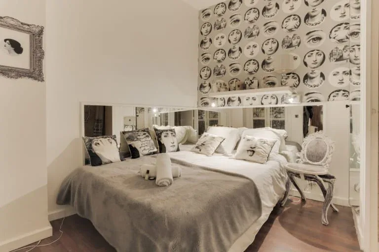 Un dormitorio con una cama grande, paneles de espejo y papel pintado con rostros.