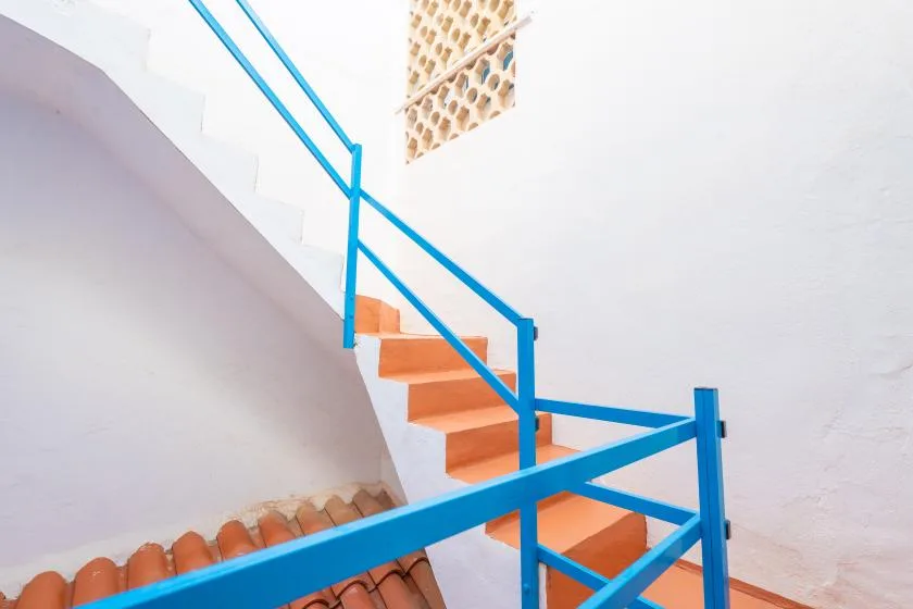 Una escalera interior con barandillas azules y peldaños color terracota.