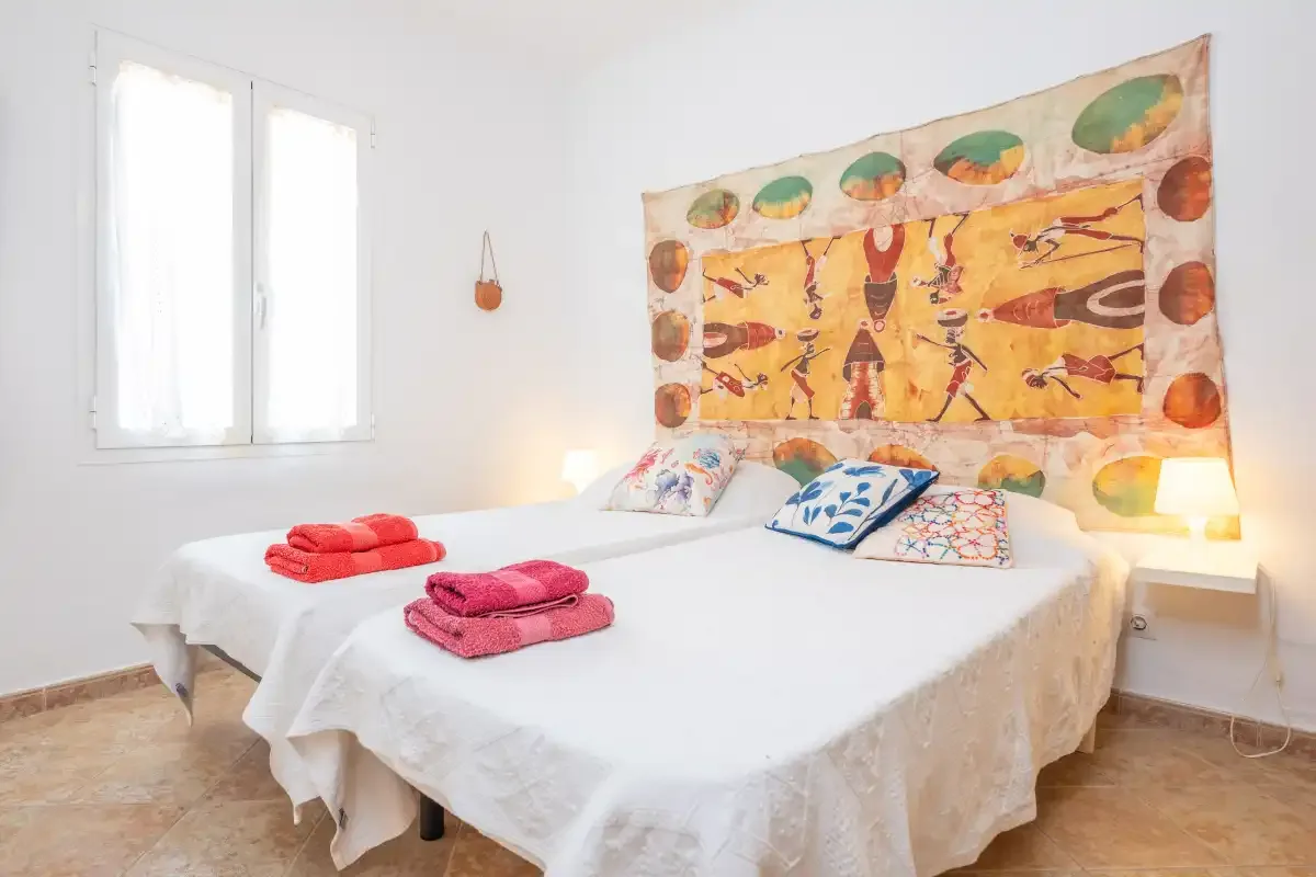 Un dormitorio con una cama blanca, almohadas de colores y un tapiz estampado.