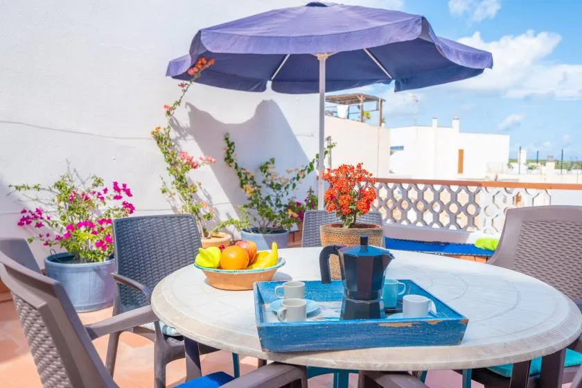 A rooftop terrace dining area with a table beneath a large umbrella.