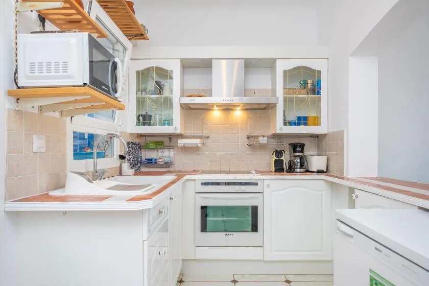 Una cocina luminosa con gabinetes blancos, salpicadero de azulejos y electrodomésticos integrados.