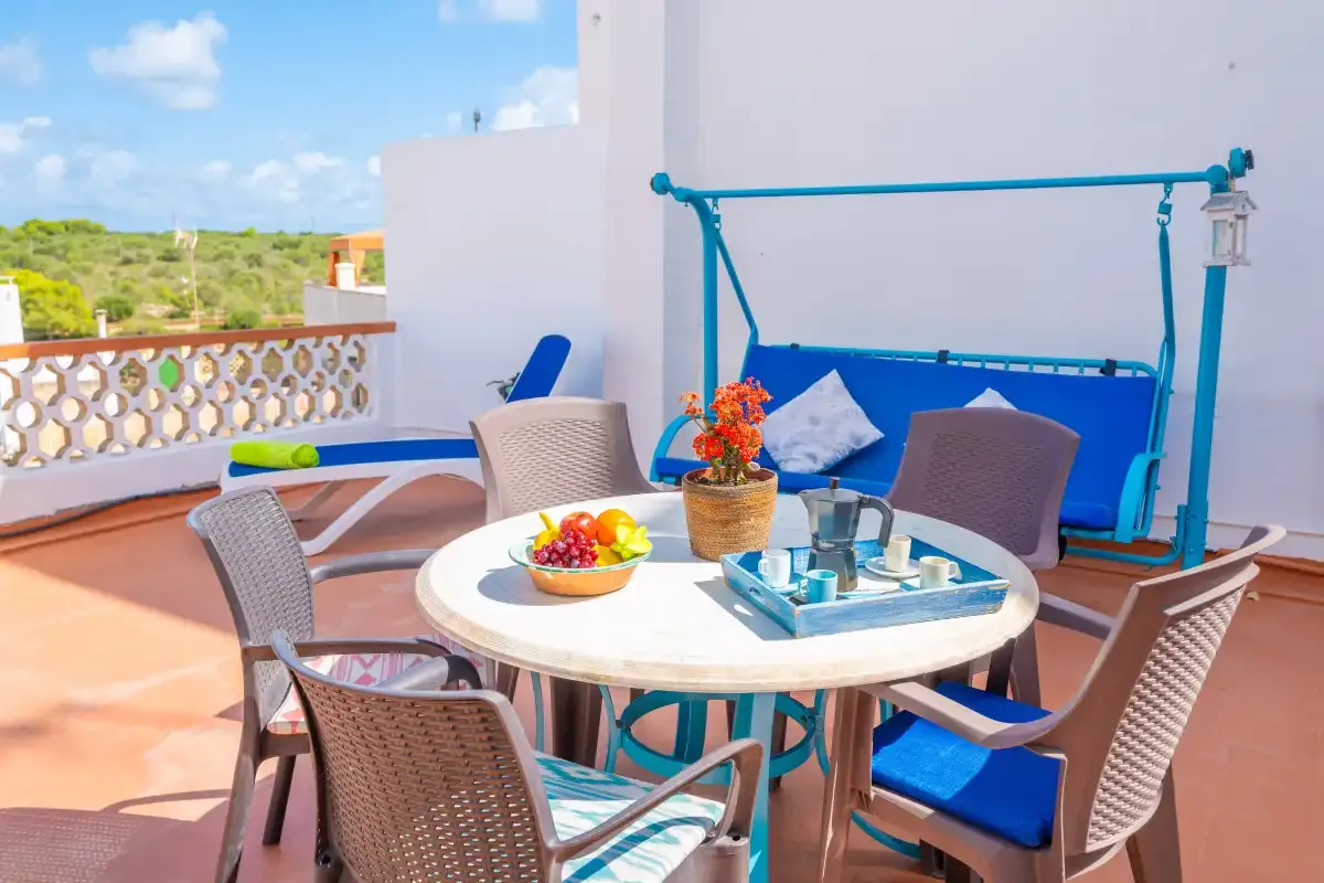 Una zona de comedor en una terraza soleada, con mesa redonda y asientos azules.