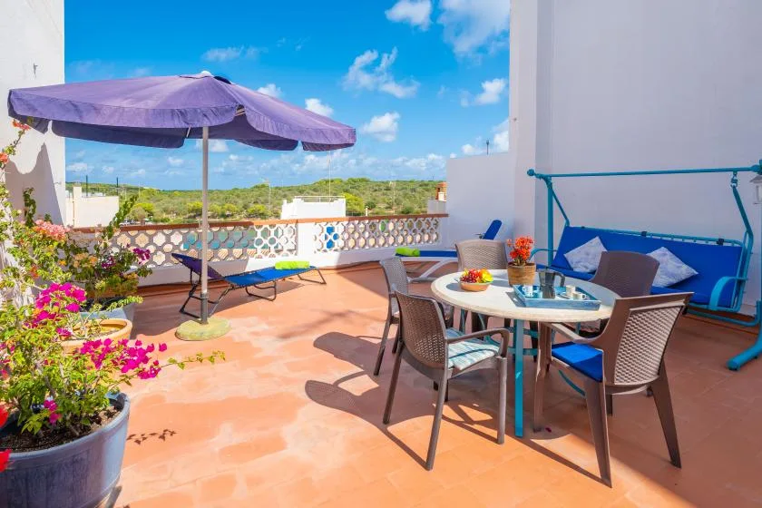 Una terraza soleada tiene una mesa de comedor, asientos al aire libre y una gran sombrilla.