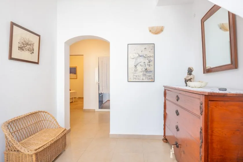 Un pasillo luminoso con un arco, asiento de mimbre y una cómoda de madera.