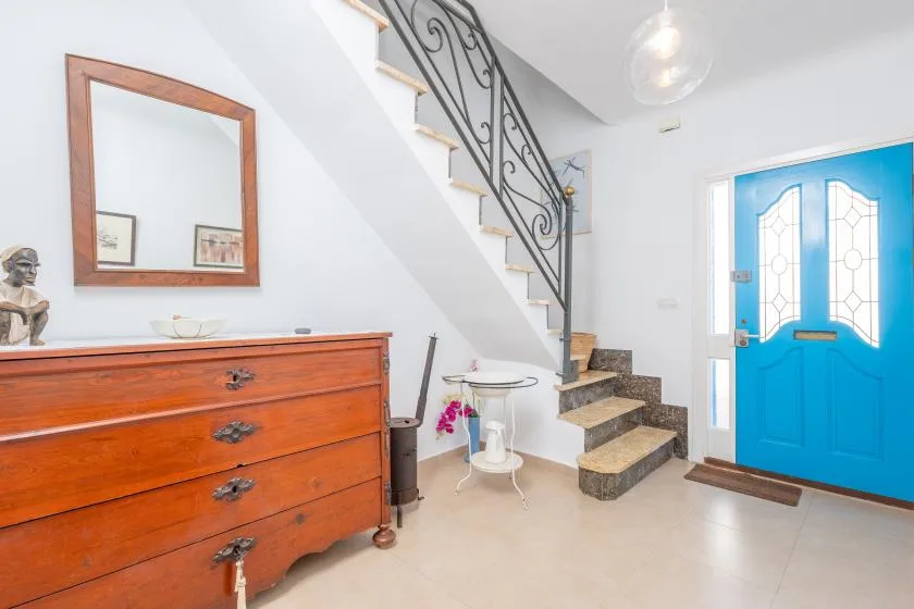 Un recibidor luminoso con una escalera, una cómoda de madera y una puerta azul.