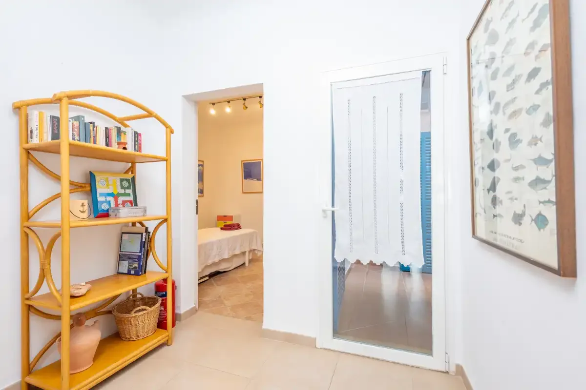 Un pasillo interior luminoso con una estantería de bambú y una puerta abierta.