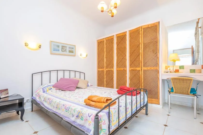 Un dormitorio con una cama de metal, ropa de cama colorida y puertas de armario tejidas.