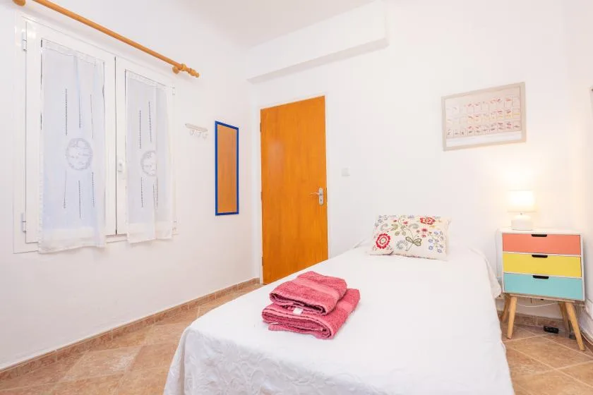 Un dormitorio luminoso con una cama, toallas de colores dobladas y una puerta de madera.