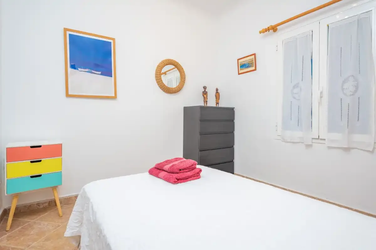 Un dormitorio con una cama bien tendida, toallas dobladas y cajones de colores.