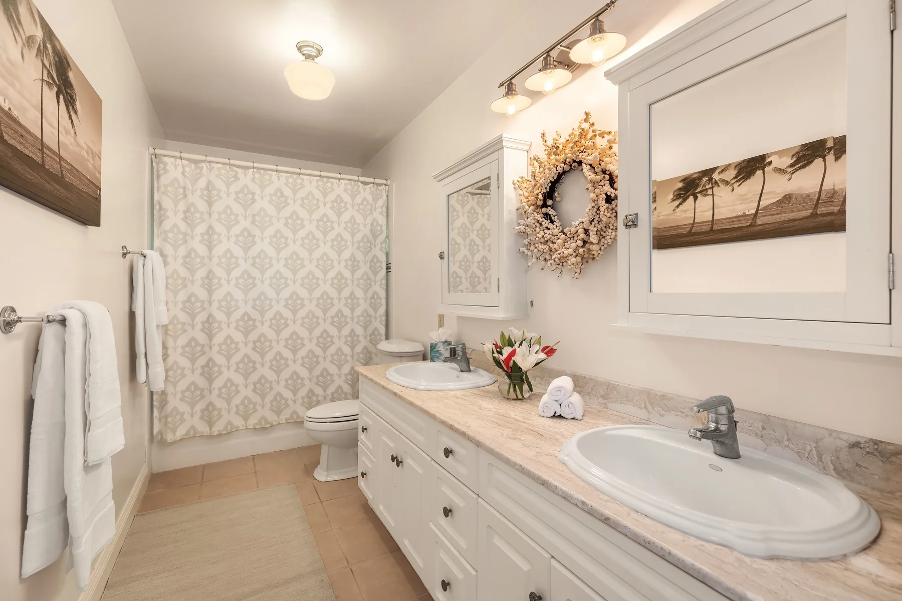 A bright bathroom with a long vanity, two sinks, and a patterned shower curtain.