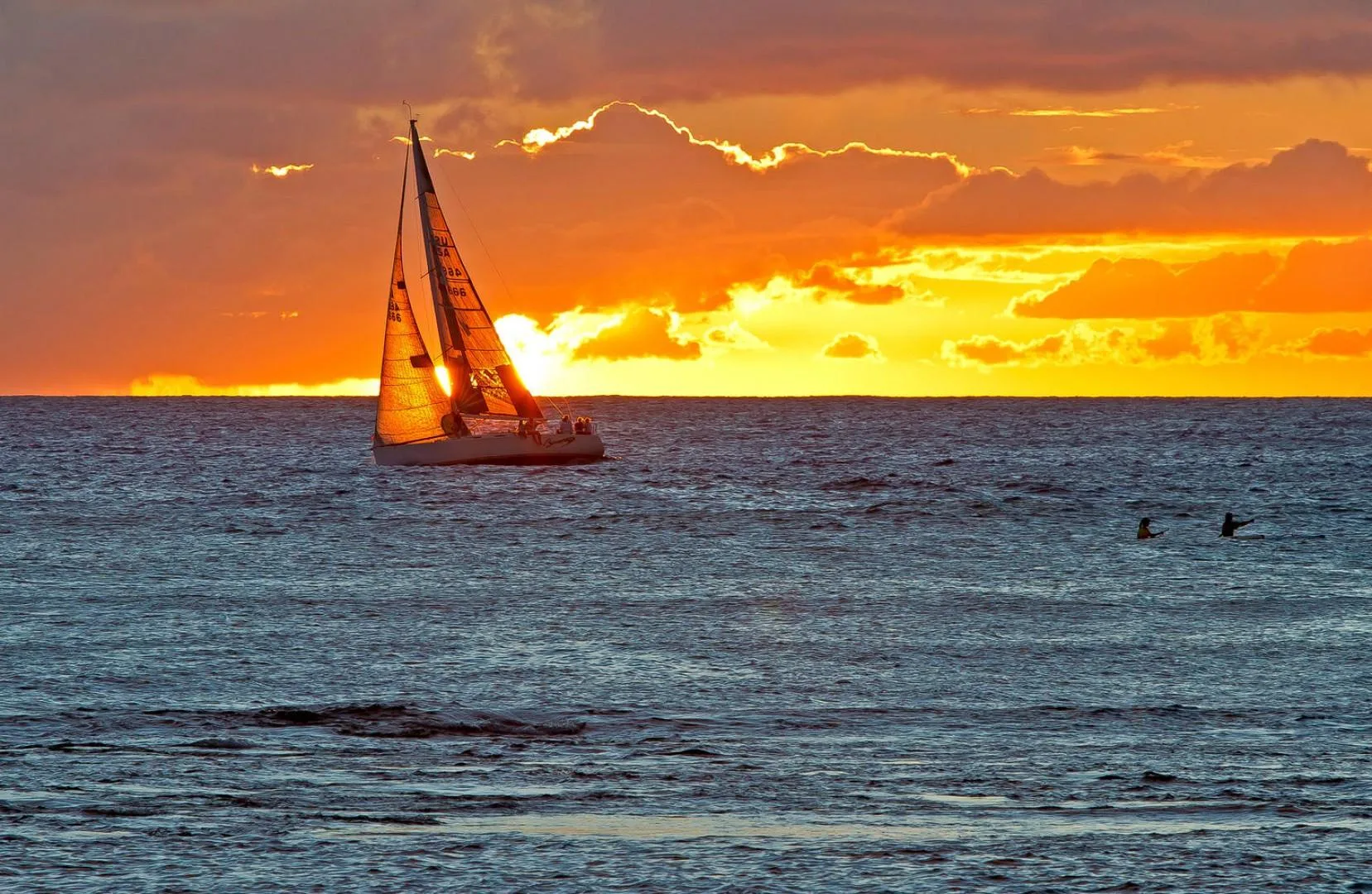 A sailboat crosses the sea beneath a glowing sunset sky.