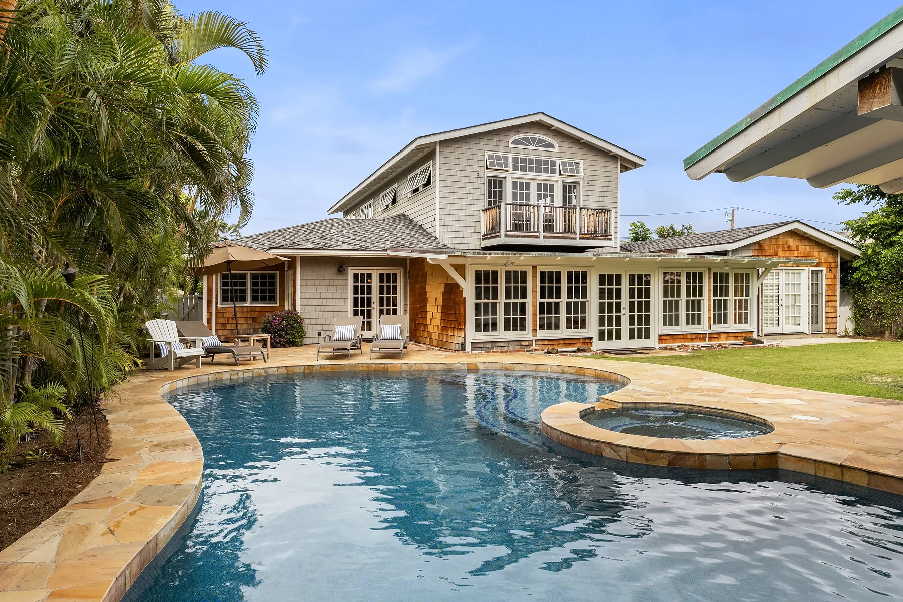 A house overlooks a swimming pool with a circular spa and a paved patio.