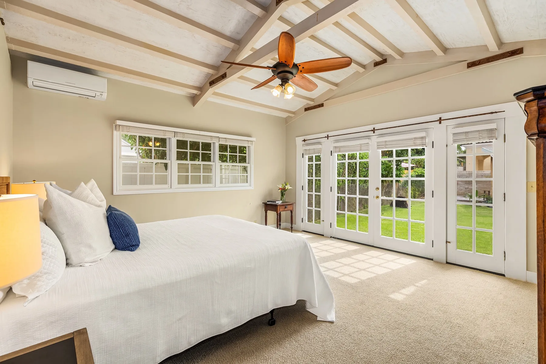 A bright bedroom with a bed, ceiling fan, and glass doors opening onto a lawn.