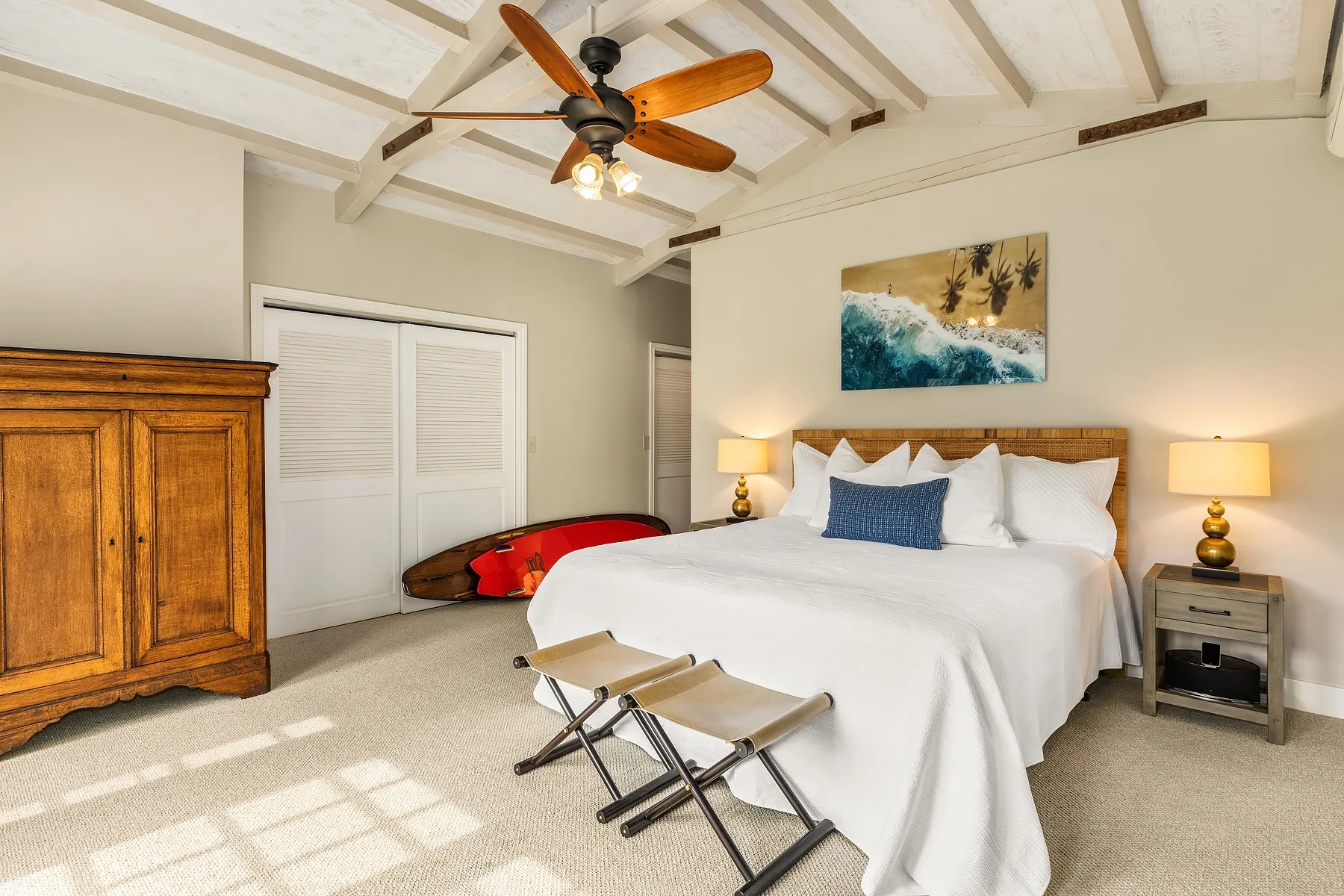 A bright bedroom with a large bed, bedside tables, and a wooden ceiling fan.