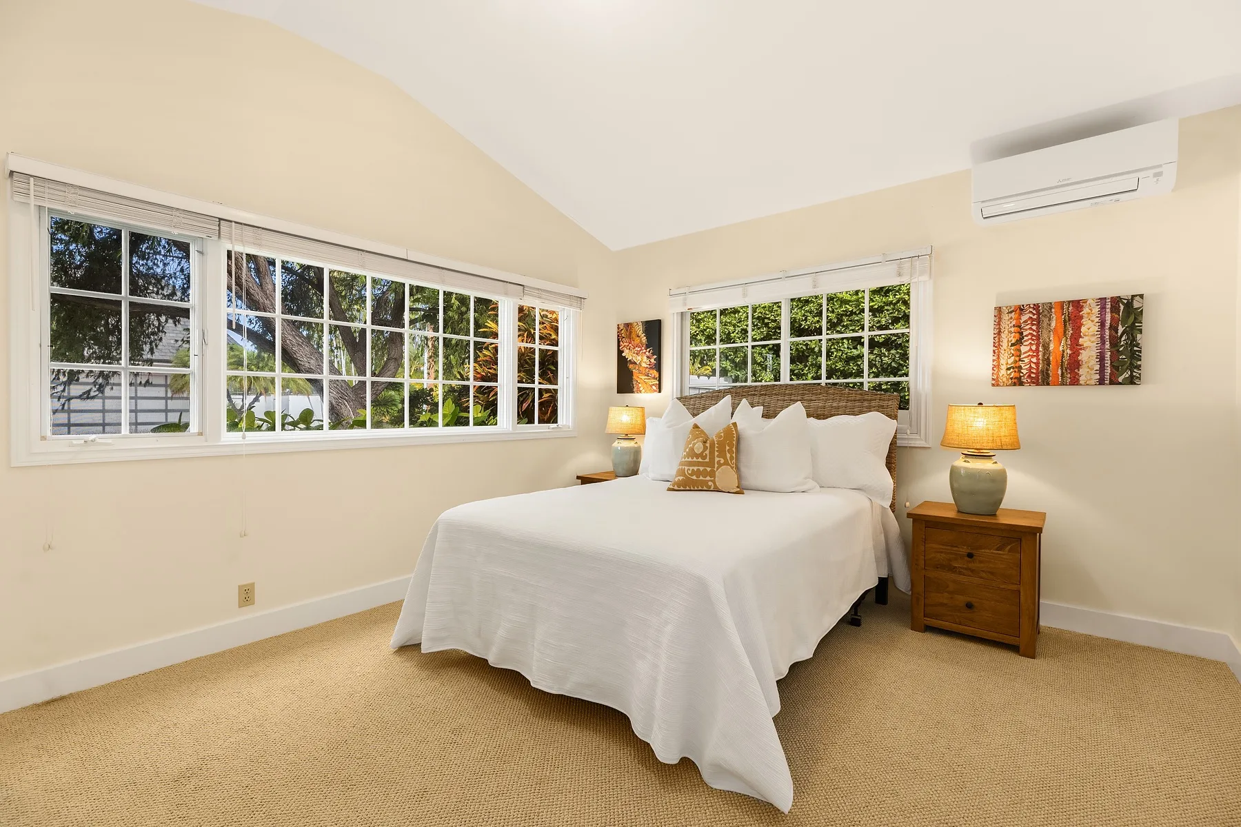 A bright bedroom with a white bed, bedside tables, and large windows.