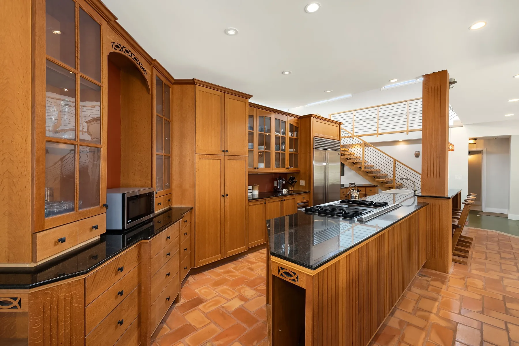 A spacious kitchen with wooden cabinetry, a central island, and a staircase in the background.
