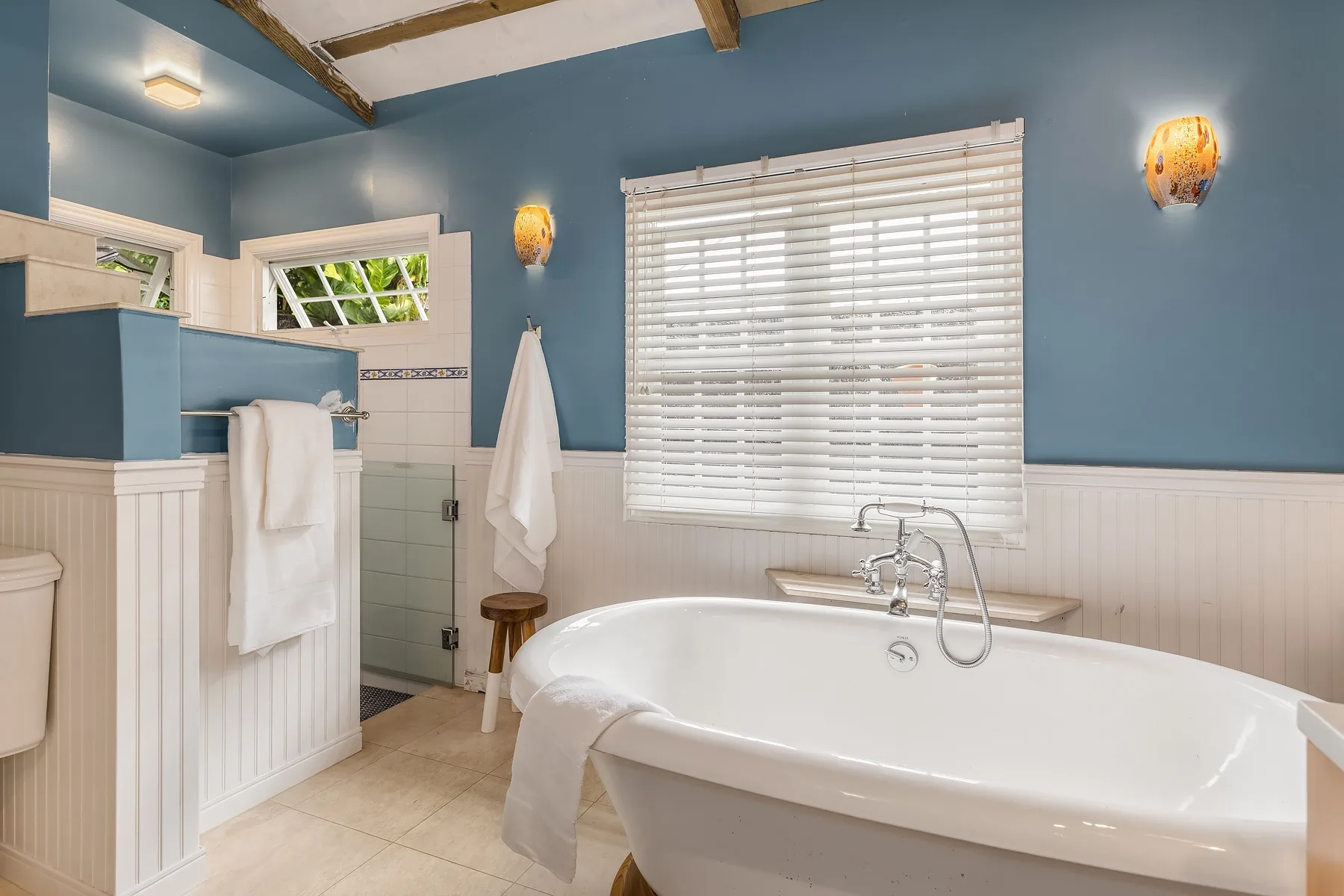 A bathroom with a freestanding bathtub, window blinds, and blue walls.