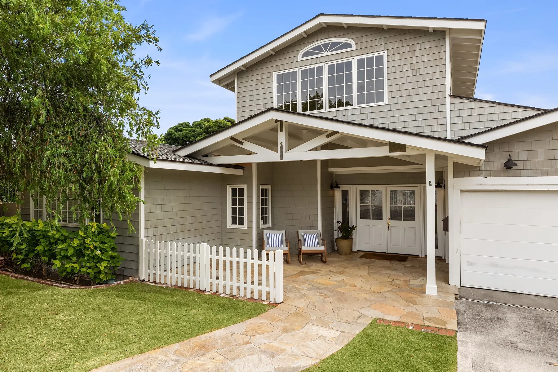 A house exterior with a covered entry, white picket fence, and stone walkway.