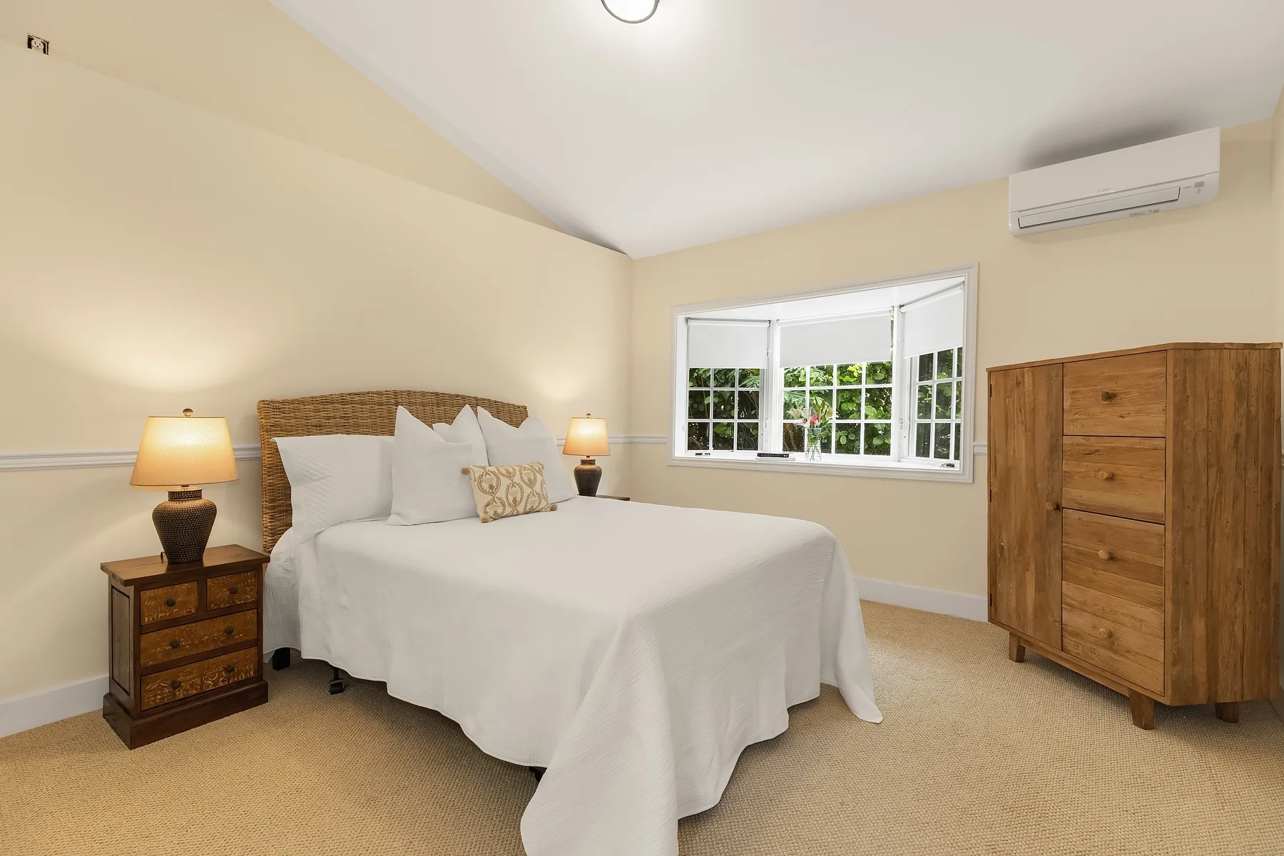 A bedroom with a neatly made bed, bedside lamps, and a wooden dresser.