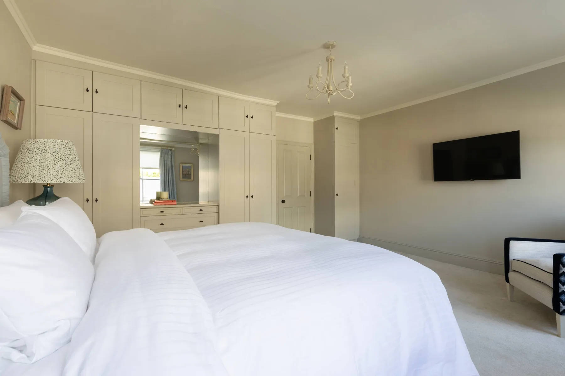 A bedroom with a white bed and a wall-mounted television.