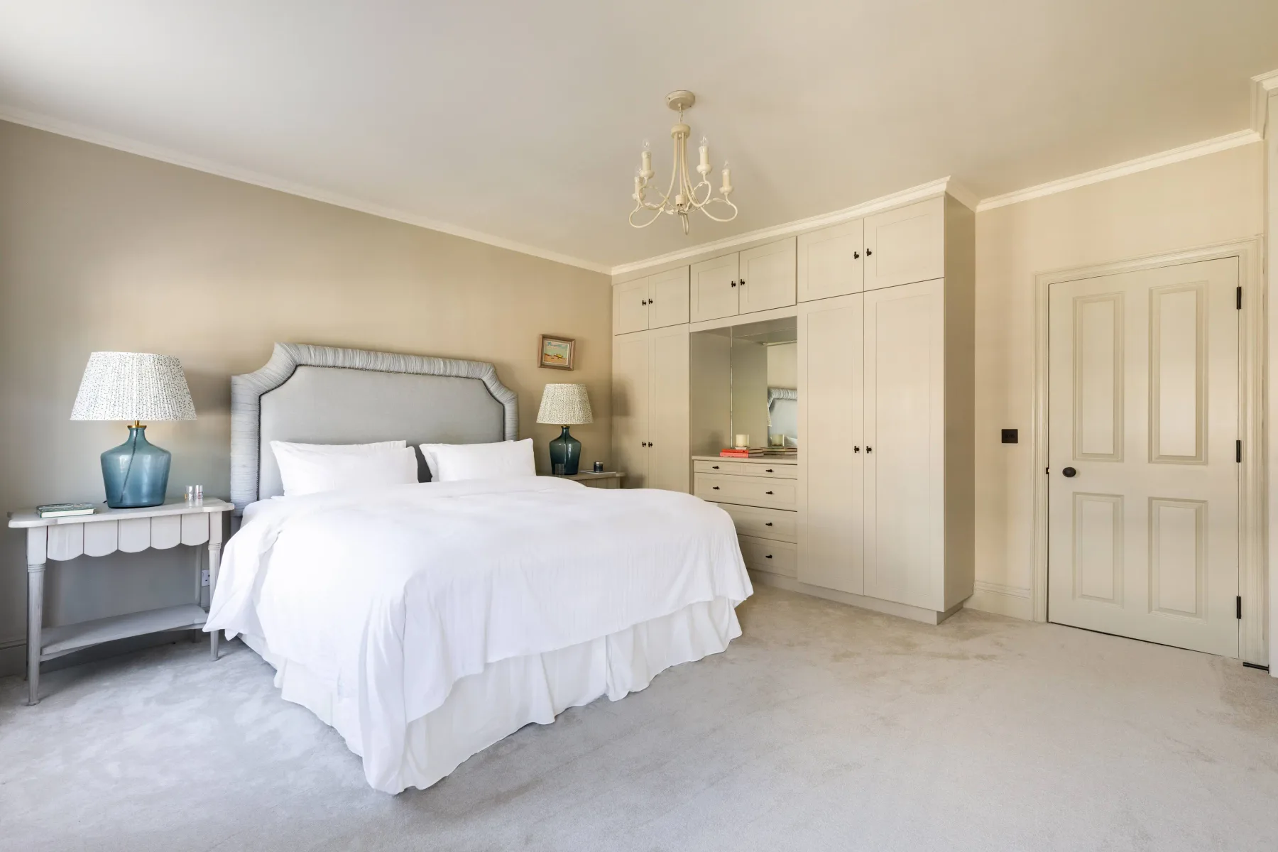 A bright bedroom with a large bed, bedside tables, and built-in wardrobes.