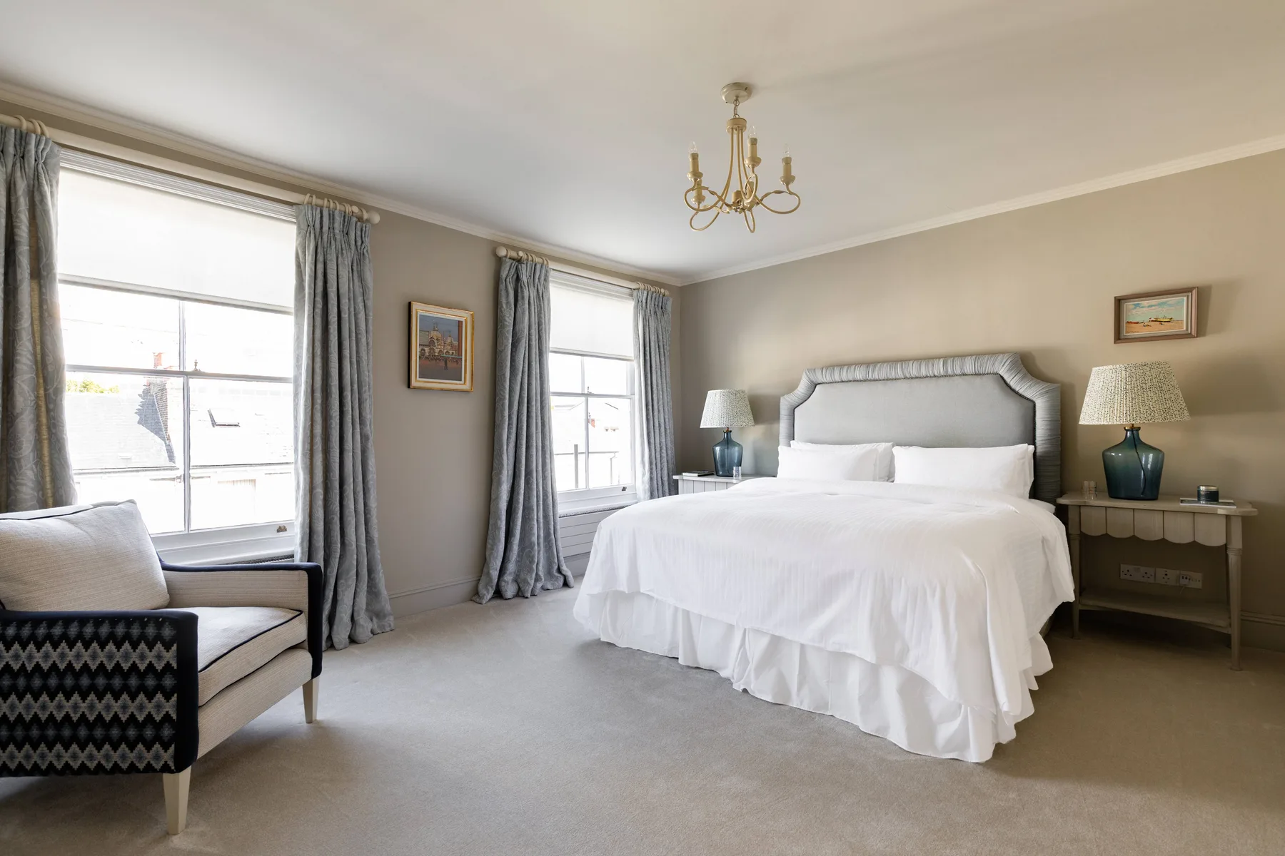 A bright bedroom with a large bed, tall windows, and gray curtains.