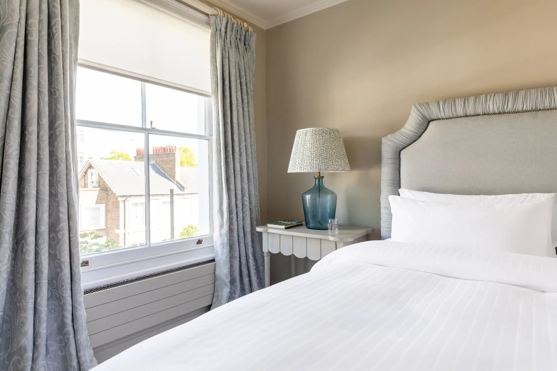 A bright bedroom with a large bed beside a curtained window.