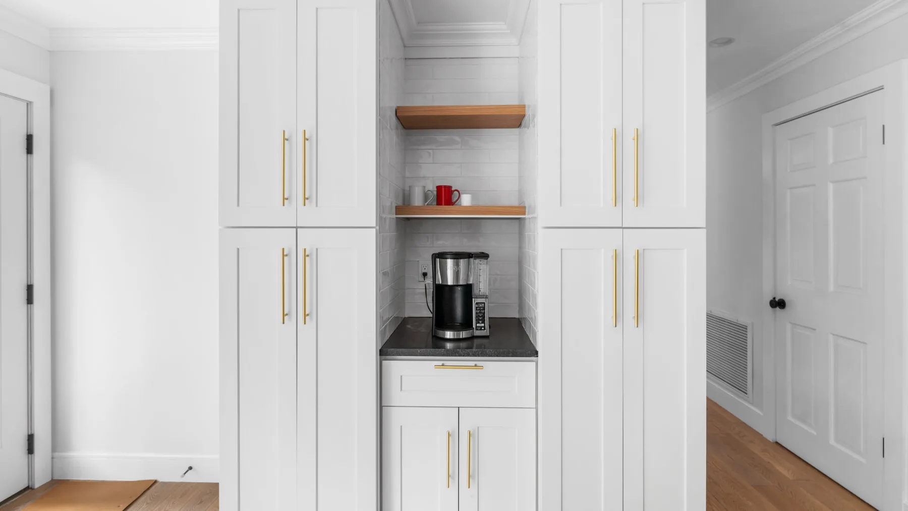 A white built-in cabinet wall includes a coffee station and wooden flooring.