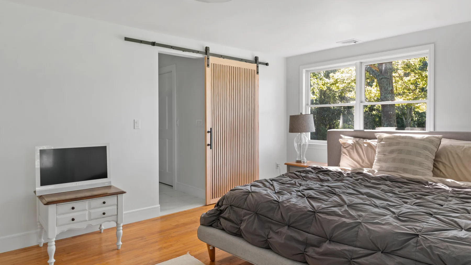 A bedroom with a bed, a window, and a sliding wood-slat door.
