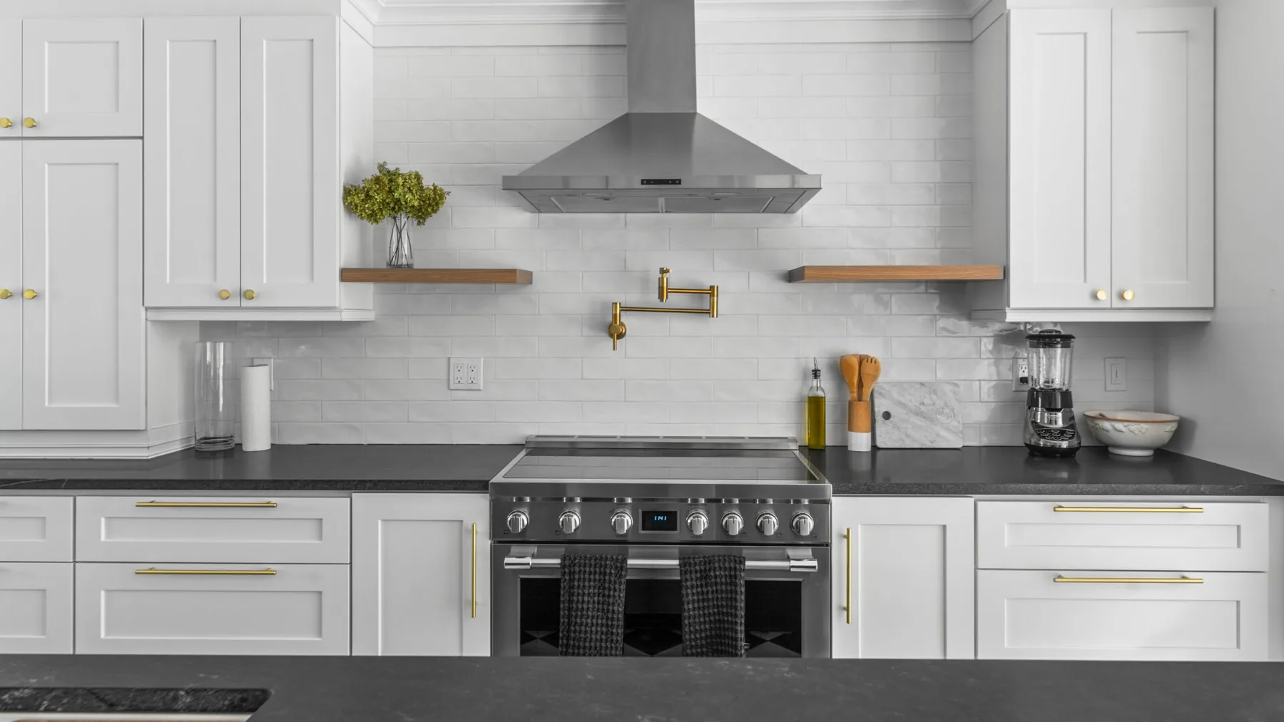 A bright kitchen with white cabinets, dark counters, and a stainless steel range.