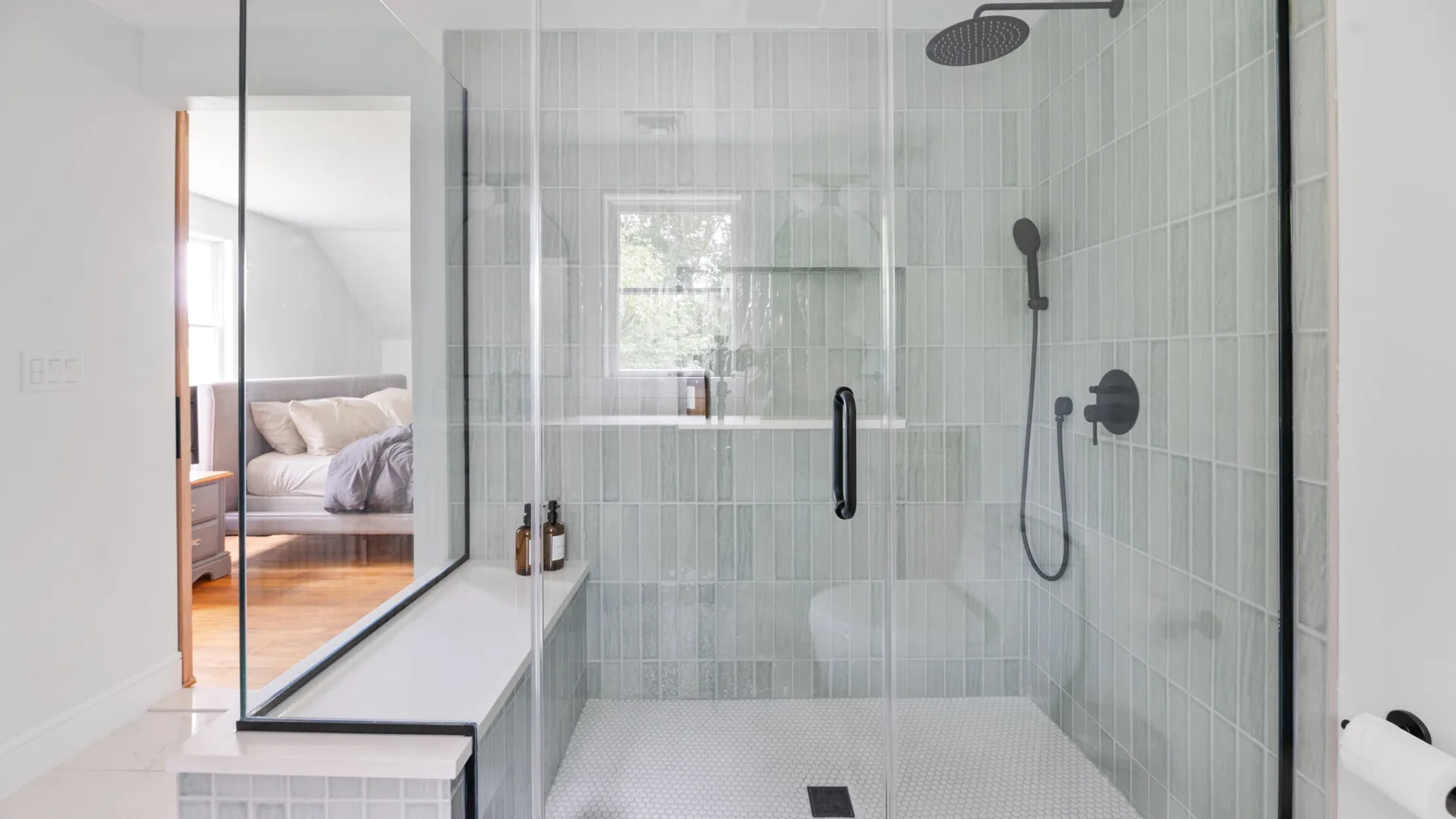 A bright tiled bathroom features a glass shower and a built-in bench.