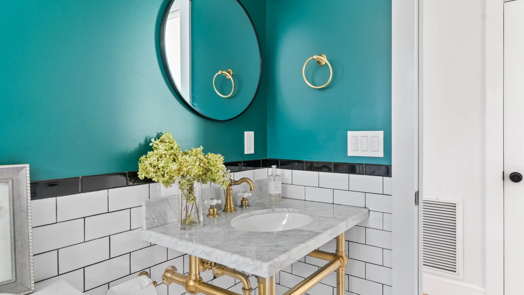 A bathroom vanity with a white sink, gold fixtures, and teal walls.