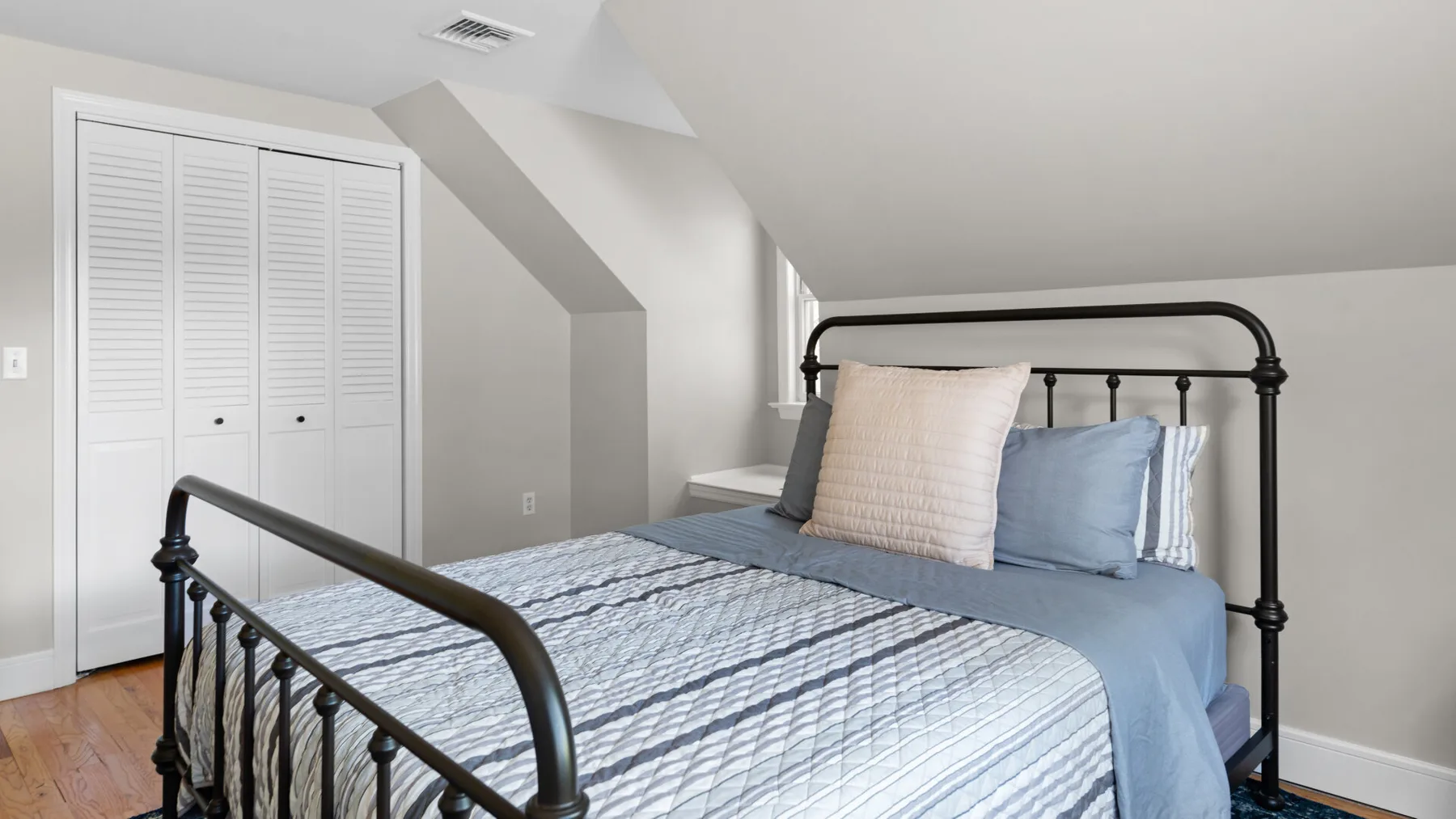 A bedroom with a metal bed, striped bedding, and a white closet.