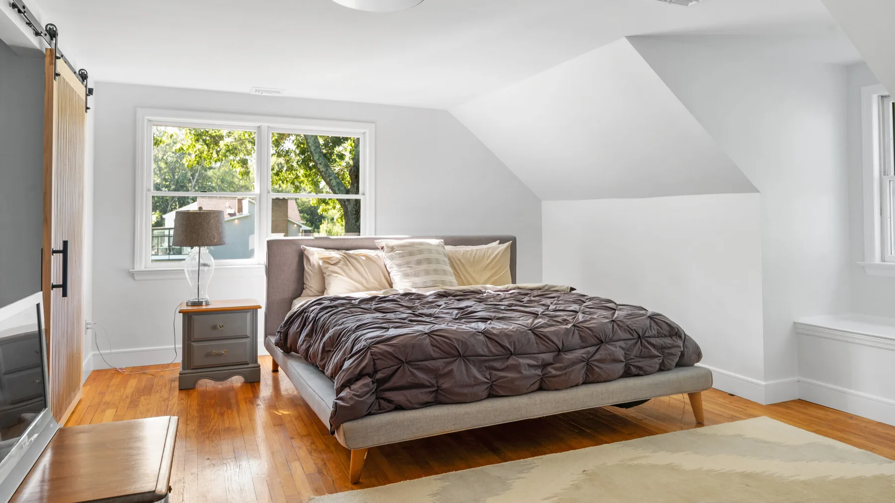 A bright bedroom with a bed beneath a sloped ceiling and windows.
