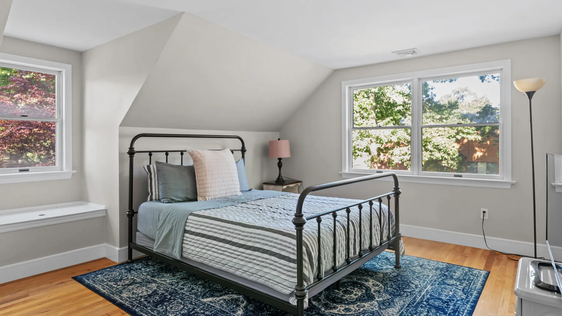 A bedroom with a metal bed, patterned rug, and windows.