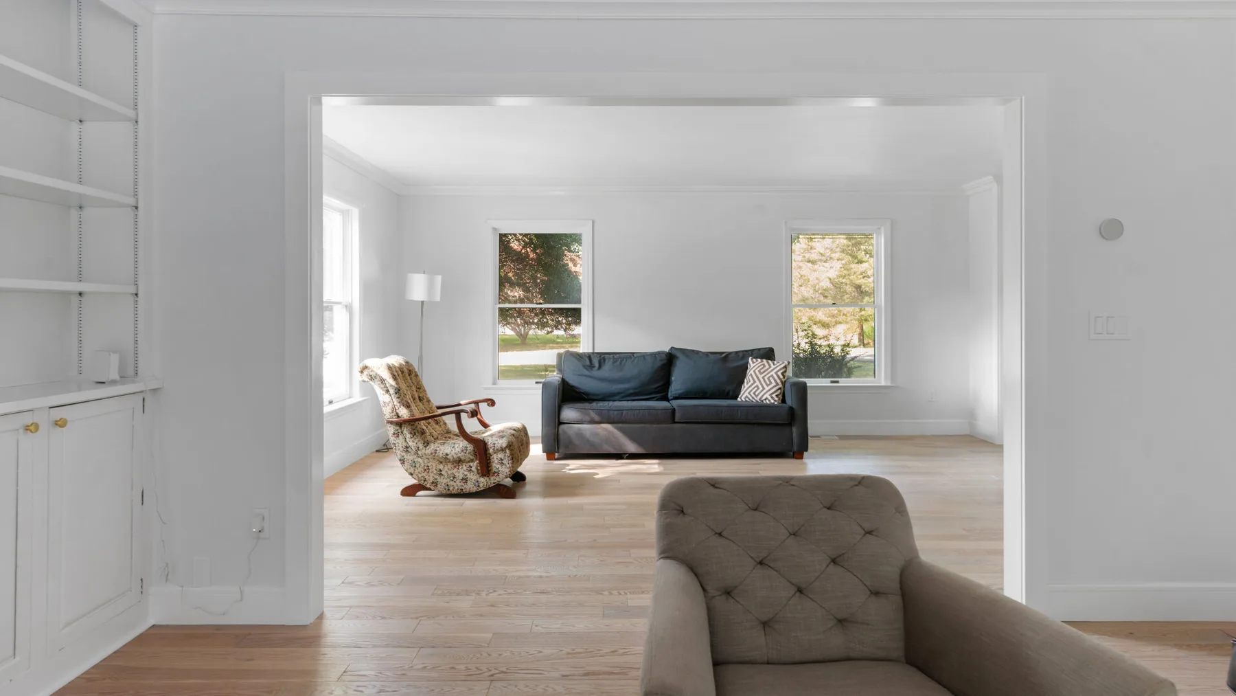 A bright living room with a dark sofa and a cushioned armchair.