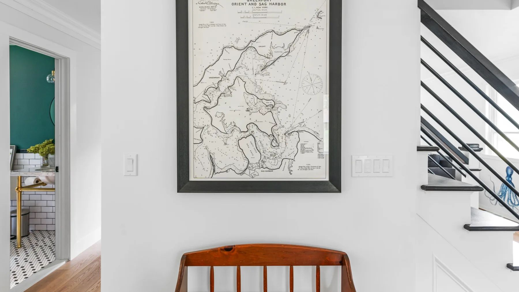 A framed map hangs above a wooden bench on a white wall.