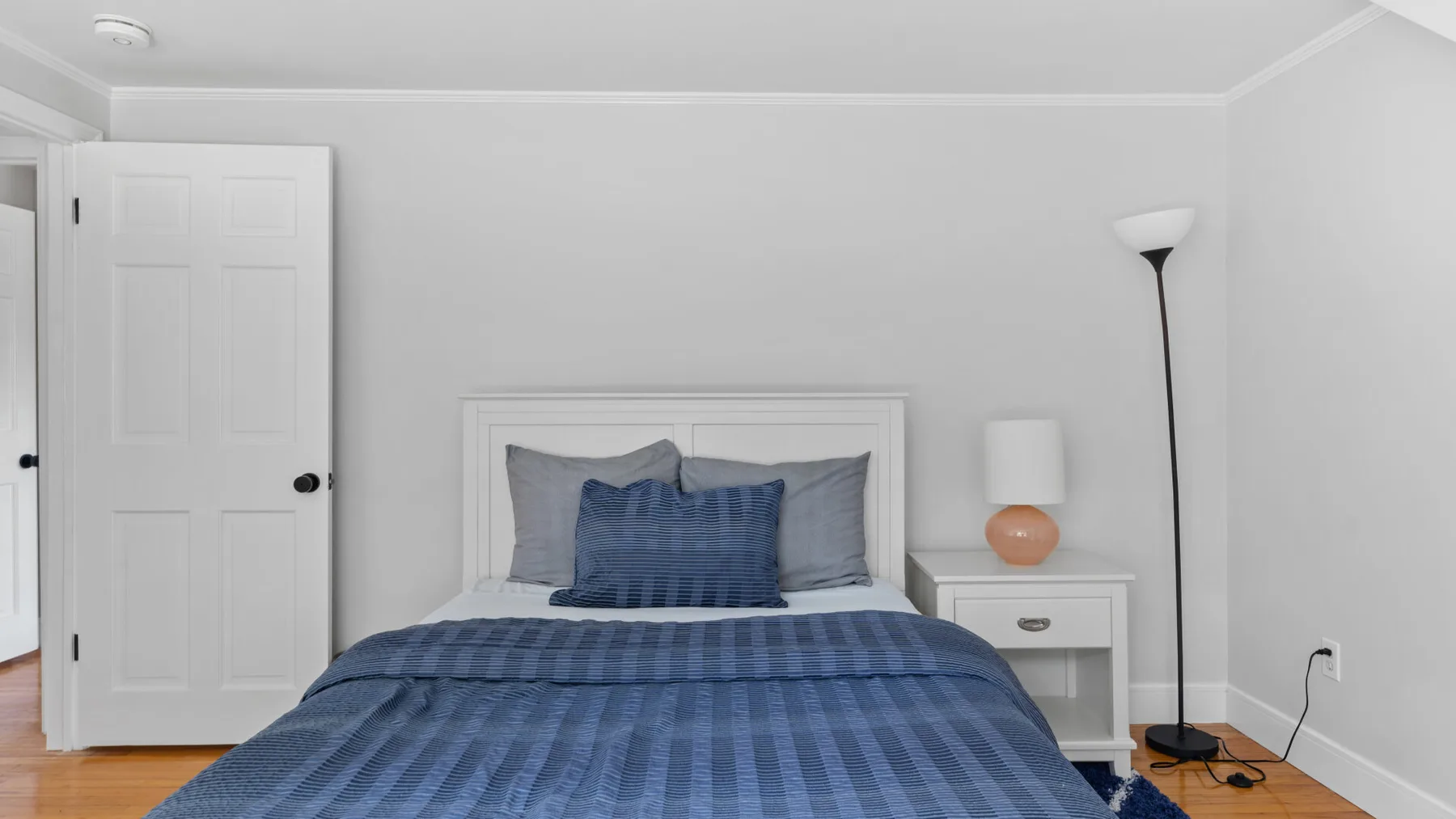 A bedroom with a bed dressed in blue bedding and a bedside table.