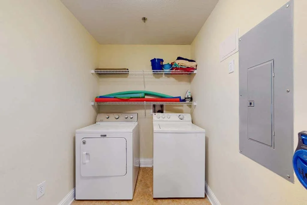 A laundry room with a washer and dryer beneath storage shelves.
